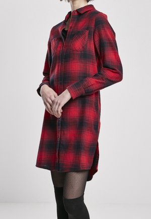 Person wearing a red and black plaid long-sleeve shirt dress with buttons and two chest pockets, paired with black fishnet tights.