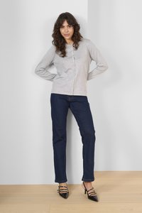 Světlá šedá kardigan s knoflíky, tmavě modré džíny a černé sandály na podpatku. Hladká textura, přiléhavý střih, ležérní styl s jednoduchými kovovými detaily.