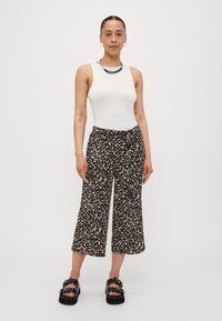 Leopard print wide-leg trousers in beige and black, with a tie waist. Paired with a white sleeveless top and chunky black sandals.