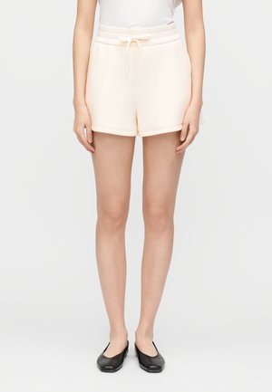 Shorts en tissu doux couleur pêche avec une taille élastique et un cordon de serrage. Coupe décontractée et ourlet lisse. Portés avec des ballerines noires.