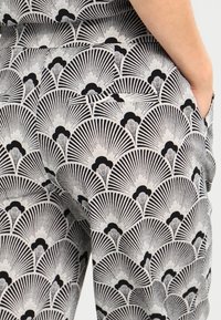 Mustavalkoinen kuviolkattoinen kangas, jossa on tuuletinaiheita säteilevin viivoin. Tekstuuriltaan se vaikuttaa sileältä, rakenteelliselta suunnittelulta ja näkyvillä taskuilla.