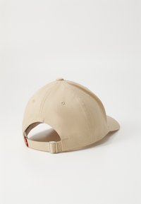 Beige katoenen baseballpet met een gebogen klep, verstelbare stoffen band en een gestikte ventilatieopening. Eenvoudig, onversierd ontwerp.