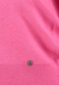 Maglione rosa lavorato a maglia con orlo a coste e una piccola targhetta in metallo nell'orlo inferiore, con motivo a cuore e testo in corsivo.