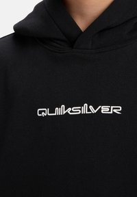 Černá mikina s kapucí a šňůrkou, na přední straně s bílým logem, s hladkou texturou látky a uvolněným střihem.