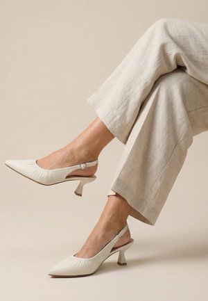 Kvinde iført beige bukser med vide ben og cremefarvede slingback-hæle med spidse tæer og en mellemhøj, skulptureret hæl.