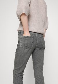 Jean en denim gris à la coupe ajustée, avec deux poches arrière et une texture légèrement délavée, associé à un pull en tricot léger.