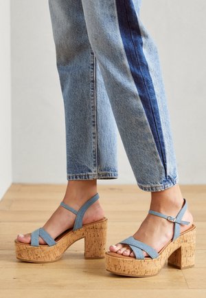 Sandalias de tacón alto azul con tiras y plataforma de corcho. Las tiras están cosidas en cruz y el tacón es grueso con un acabado texturizado de corcho.