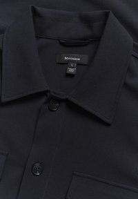 Tumedat sinine särk säädkeel koos nupuga ees, kahe rinna tasku ja kraega. Kanga tekstuur on sile, sisaldades peeneid õmblusteadlikkusi. Suurus L.