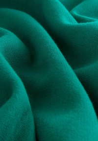Material moale, pliat de culoare teal, cu textură de tricot vizibilă și umbre delicate care pun în evidență suprafața sa netedă și comfortabilă.