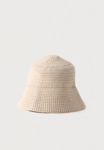 Μπεζ καπέλο τύπου bucket, πλεκτό με βελονάκι, με στρογγυλεμένη κορυφή και ελαφρώς φαρδιά γείσο σε απλό ανοιχτό φόντο.