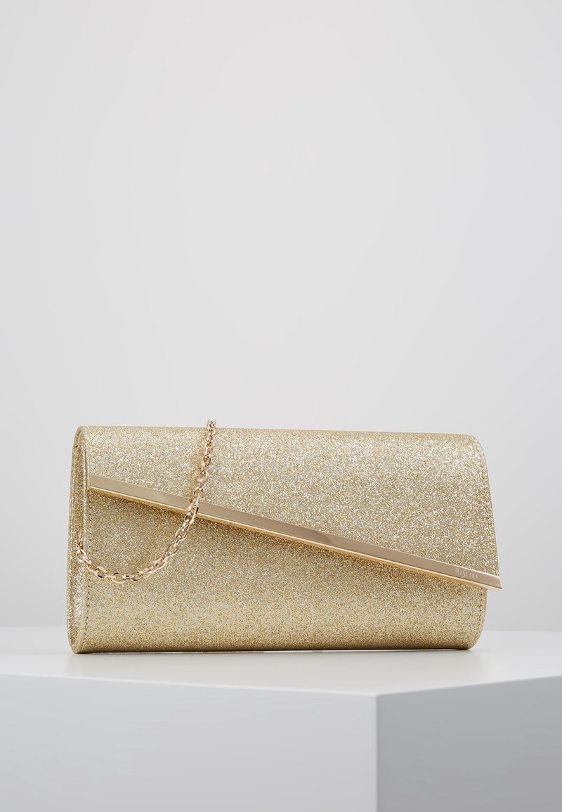 Pochette à paillettes dorées avec barre métallique diagonale et bandoulière chaîne reposant sur une surface blanche sur fond gris clair.