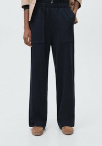 Navy wide-leg trousers made from soft fabric with an elastic waistband, featuring two large front pockets and a smooth texture.