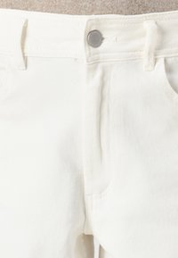 White denim jeans feature a classic five-pocket design, front button, and a zip fly. The fabric has a smooth texture.
