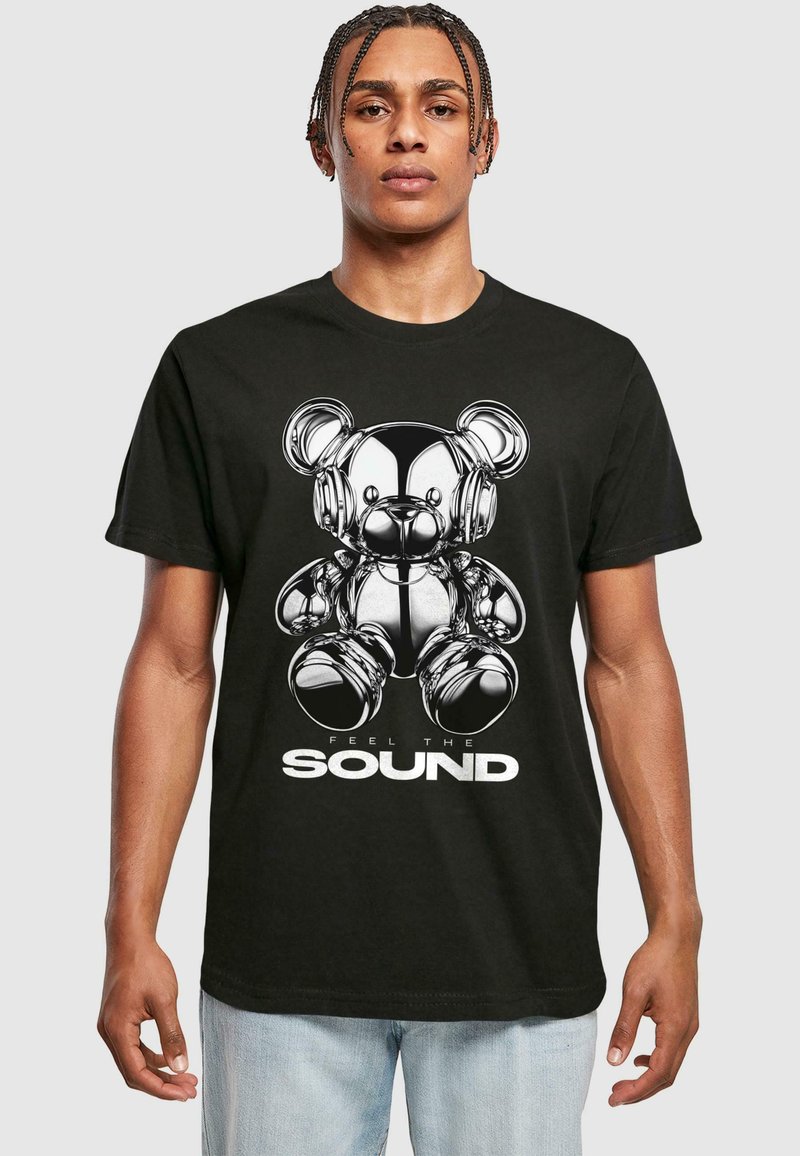 Svart t-skjorte med et trykk av en metallisk kosedyr med hodetelefoner, ledsaget av teksten "FEEL THE SOUND" i hvitt.