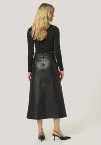 Musta nahkainen midihame, jossa on sileä pinta, korkea vyötärö ja saumaan liittyviä yksityiskohtia, yhdistettynä mustiin korollisiin slingback-kengiin.