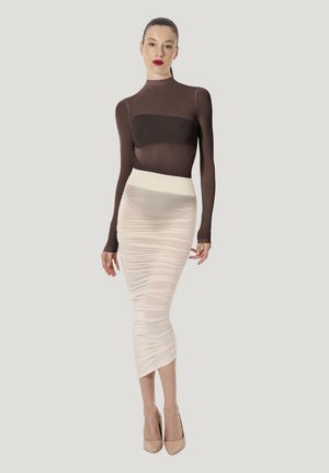 Brun genomskinlig tröja med långa ärmar kombinerad med en figursydd, rynkad krämfärgad kjol, markerad med en hög midjeband och ihopparad med nudefärgade högklackade skor.
