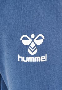 Blaues Gewebe mit einem strukturierten Muster und einem weißen Hummel-Logo. Das Design beinhaltet eine abstrakte Form über dem Markennamen.