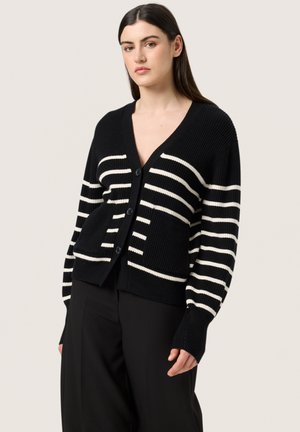 Randig svart och vit cardigan i ribbat stickat material, med V-ringning, knäppning fram och två framfickor. Långa ärmar med texturerad detalj.