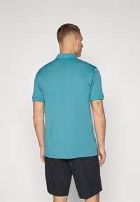 Turkizna polo majica s kratkimi rokavi, teksturirana tkanina in ovratnik. Usklajeni akcenti v turkizni barvi in sproščen kroj. Nosi se z črnimi kratkimi hlačami.