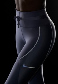 Vysoko pasové, tmavě námořnické legíny s reflexním prošíváním a malým logem Nike. Materiál vypadá hladce a přiléhavě.