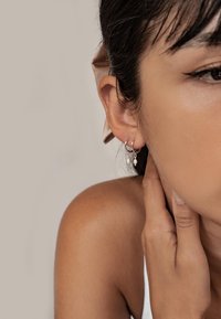 Boucles d'oreilles créoles en argent ornées de petites perles blanches pendantes. Gros plan sur l'oreille, mettant en valeur le design des boucles et leurs détails délicats.