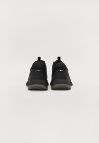 Baskets de sport noires avec un design texturé, semelle épaisse et languettes au talon. Des accents de logo discrets sont présents à l'arrière.
