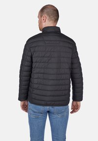 Sort pufferjakke med vandret syninger, høj krave og lange ærmer, båret over blå jeans. Blødt, let materiale.