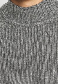 Maglione grigio a collo alto realizzato in maglia, con texture a coste e colletto aderente. Il tessuto presenta un delicato motivo intrecciato.
