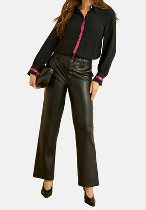 Kobieta w czarnych, szerokich spodniach ze skóry, czarnej bluzce z długim rękawem ozdobionej różowym cekinowym wykończeniem, trzymająca czarną kopertówkę, w czarnych szpilkach.