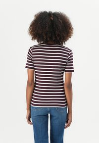Bordeauxrode en witte gestreepte shirt met korte mouwen. Zachte stof met een getailleerd ontwerp. Gepaard met blauwe denim jeans, wat een casual uitstraling geeft.