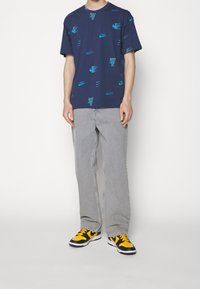 Navy blue T-shirt with turquoise Nike logos and "Just Do It" text, paired with light gray jeans and black-yellow sneakers.