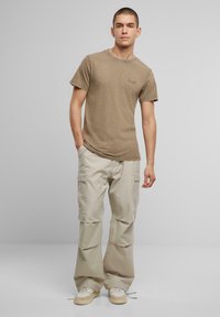 Brun bomulds T-shirt med korte ærmer og et diskret logo på brystet, parret med lyse beige cargo-bukser med flere lommer og en afslappet pasform.