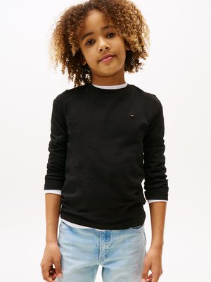 Sort langærmet skjorte med detaljer i hvid krave, parret med lysblå denimjeans. Skjorten har et lille logo på brystet.