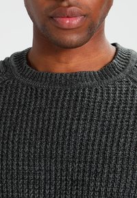 Mörkgrå stickad tröja med rund halsringning och ribbad textur, med synliga sömmar och en avslappnad passform.