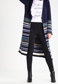 Długi granatowy kardigan z dzianiny z wielokolorowymi paskami, w połączeniu z czarnymi spodniami slim fit i botkami za kostkę. Posiada luźny krój.
