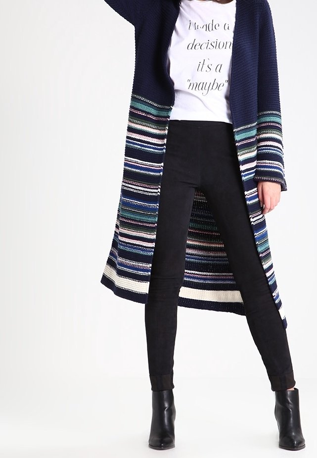 Długi granatowy kardigan z dzianiny z wielokolorowymi paskami, w połączeniu z czarnymi spodniami slim fit i botkami za kostkę. Posiada luźny krój.