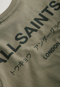 Oliwkowa zielona koszulka z okrągłym dekoltem, z wyraźnym czarnym napisem: "ALLSAINTS" oraz japońskimi znakami, wykonana z miękkiej bawełny.
