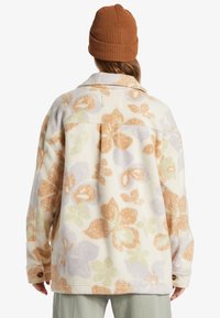 Fleece jacket with floral pattern in pastel colors (orange, purple, green) and a relaxed fit. Features a collar and buttoned cuffs.