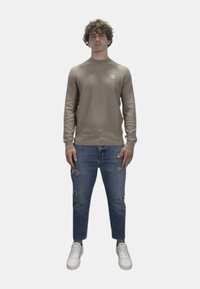 Maglione a maniche lunghe color beige chiaro con un motivo testurizzato, abbinato a jeans blu strappati e sneakers bianche. Design semplice, vestibilità rilassata.
