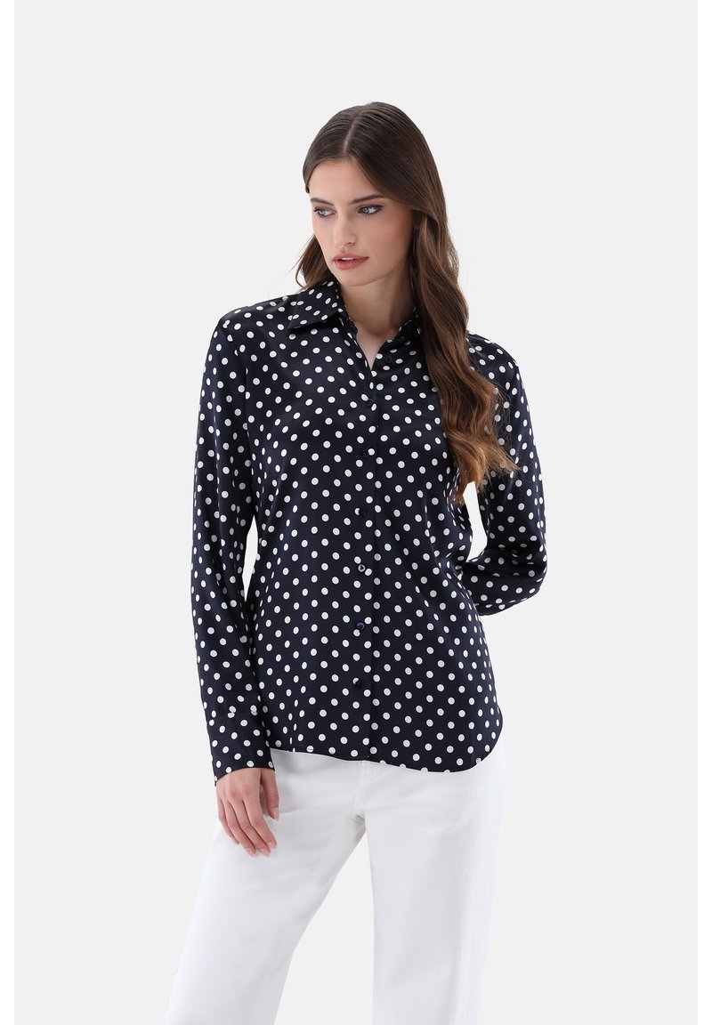 Navy blue polka dot button-up shirt with long sleeves, collar, and smooth texture, paired with white trousers. Polka dots are white.