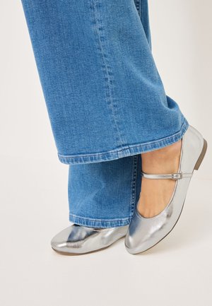 Metallisch zilveren balletschoenen met een enkelbandje, gedragen met wijdvallende blauwe denim broek. Gladde textuur, ronde neus, minimalistisch ontwerp.