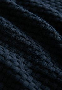 Dunkelblauer gewebter Stoff mit strukturiertem Muster, das erhabene Quadrate und ein weiches, gestricktes Aussehen aufweist.