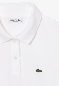 Weißes Polohemd mit klassischem Kragen, dreiknöpfiger Knopfleiste und strukturiertem Stoff. Mit kleinem grünen, gesticktem Krokodil-Logo.