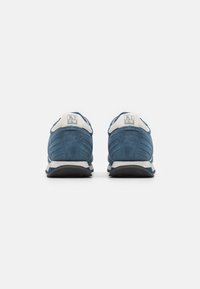 Scarpe sportive in suede blu con accenti bianchi, fondo arrotondato e suola texturizzata. Logo sul retro, caratterizzato da un design semplice.