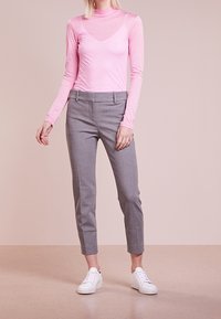 Roze lange mouwen top met transparante delen, gecombineerd met grijze op maat gemaakte broeken en witte sneakers, die een strakke, moderne silhoutte laat zien.