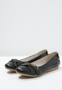 Czarne baletki skórzane z plecionymi detalami z przodu, okrągłym noskiem oraz płaską, brązową podeszwą z delikatnym logo z boku.