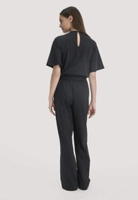 Schwarzer Jumpsuit mit lockerer Passform, kurzen Ärmeln und einem Schlüsselrücken-Detail. Glatte Textur und weit geschnittene Beine, ideal für Komfort.