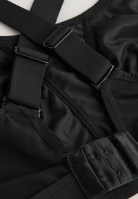 Schwarzer Sport-BH mit verstellbaren Trägern, Netzdetails und Haken-Ösen-Verschluss. Hergestellt aus dehnbarem, glattem Material.