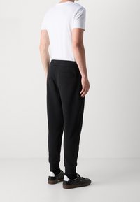 Svarta tapered sweatpants med elastiskt midjeband, sidfickor och en bakficka, kombinerat med en vit t-shirt med rund hals och svarta sneakers.