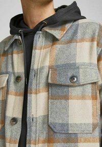 Giacca camicia in lana a quadri beige, grigia e arancione. Presenta due tasche sul petto, chiusure a pulsante e una consistenza di peso medio.